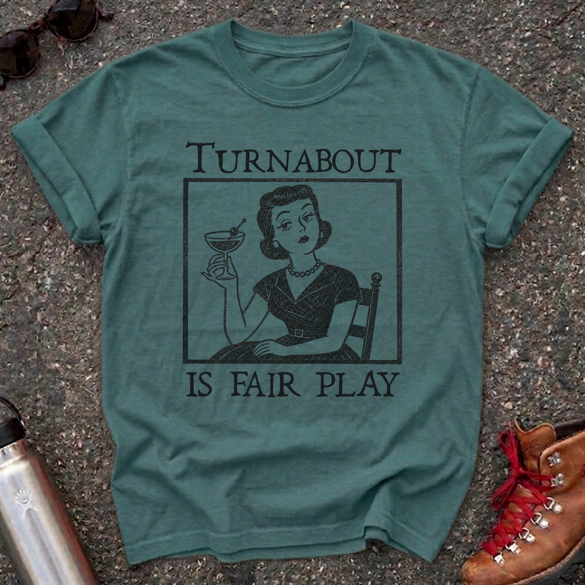 Comfort Colors t-shirt with a retro 1950s housewife holding a martini in vintage woodcut style and the words Turnabout Is Fair Play