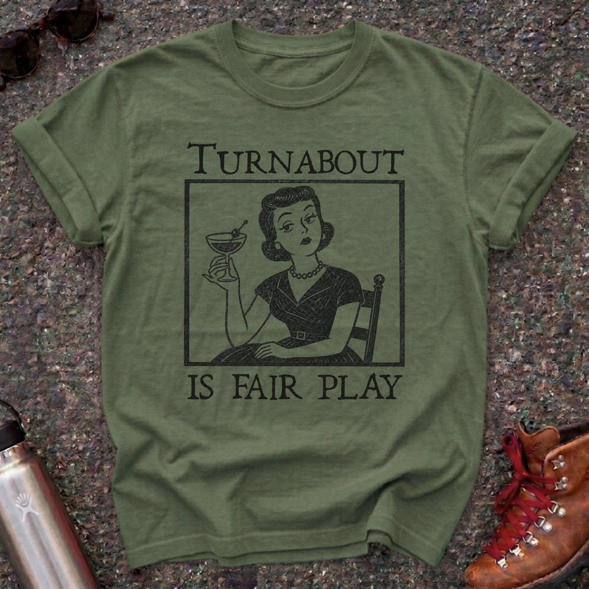 Comfort Colors t-shirt with a retro 1950s housewife holding a martini in vintage woodcut style and the words Turnabout Is Fair Play